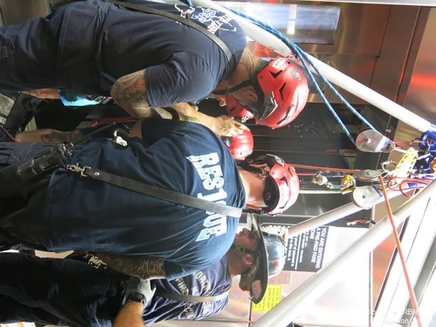The second victim to be rescued from a stuck light rail elevator, second from left, takes off his red helmet after North Hudson firefighters  brought  him up to street level, where he was turned over to EMS for examination.  